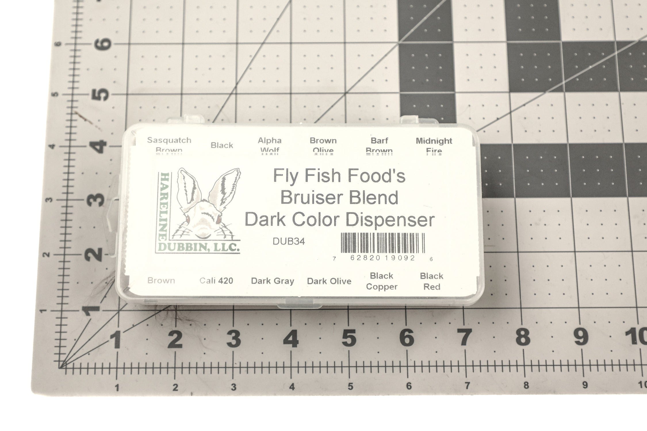 White plastic Bruiser Blend dark dubbing dispenser with Hareline rabbit logo on gridded mat, fly tying materials