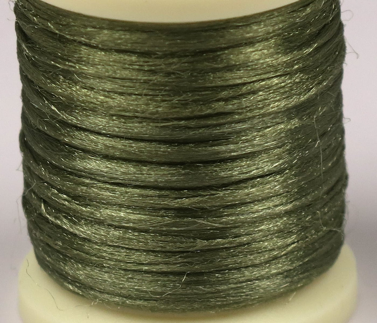 Close-up spool of Hareline Antron yarn in olive green, shiny synthetic fibers wrapped on a white plastic fly-tying spool