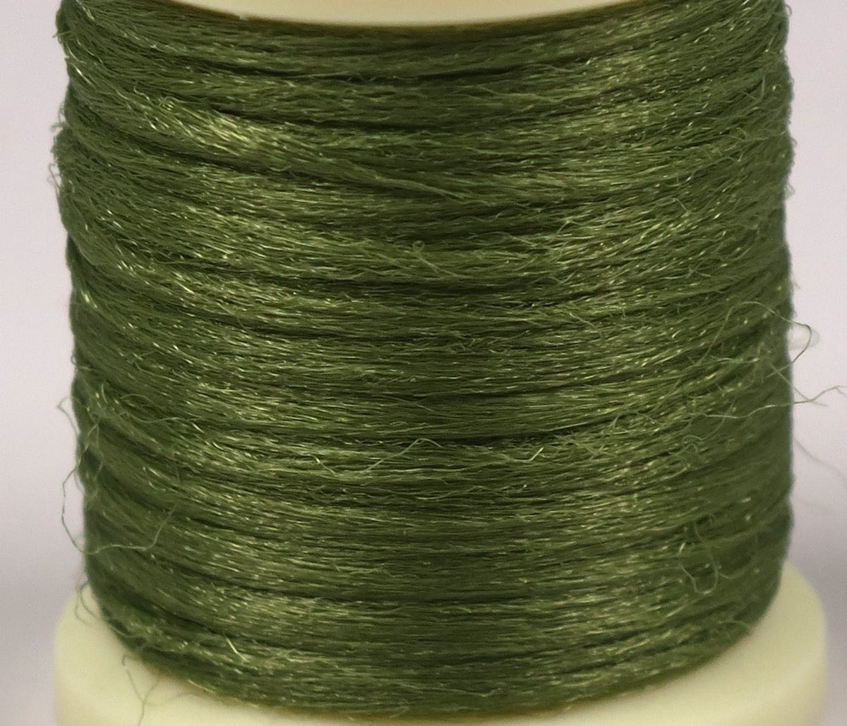 Hareline Antron yarn spool in olive green, shiny synthetic fibers for fly tying, fine textured filament wound on spool