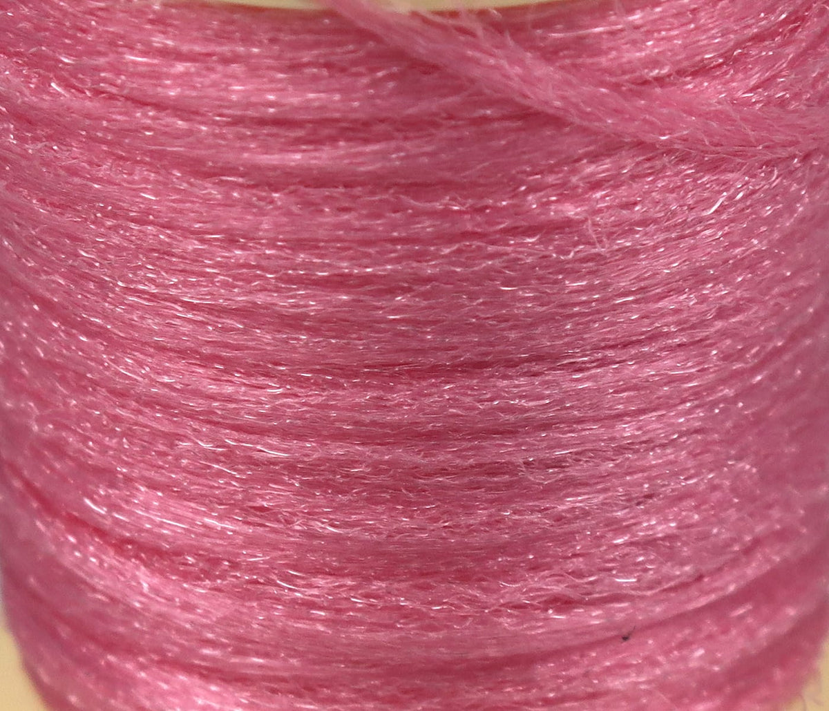 Close-up of Hareline Antron pink synthetic yarn spool with fine shimmering fibers for fly tying