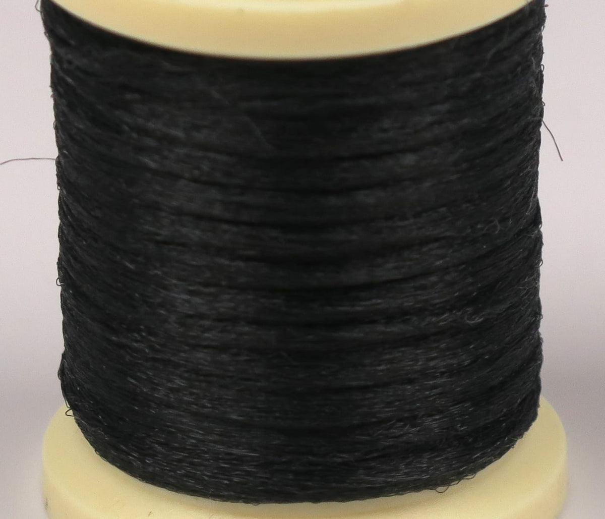 Black Hareline Antron yarn spool with fine synthetic fibers wrapped tightly on a cream plastic base, fly tying material