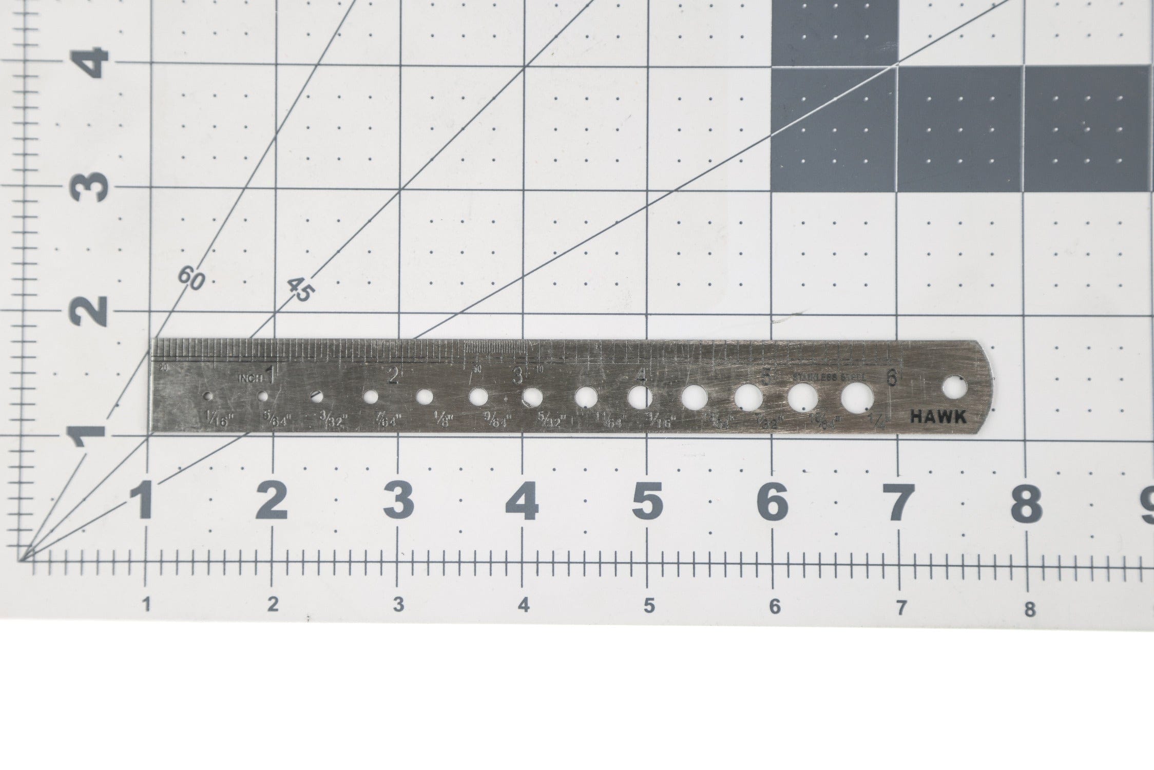 Silver stainless steel bead sizer ruler with engraved inch markings and round sizing holes on white gridded mat