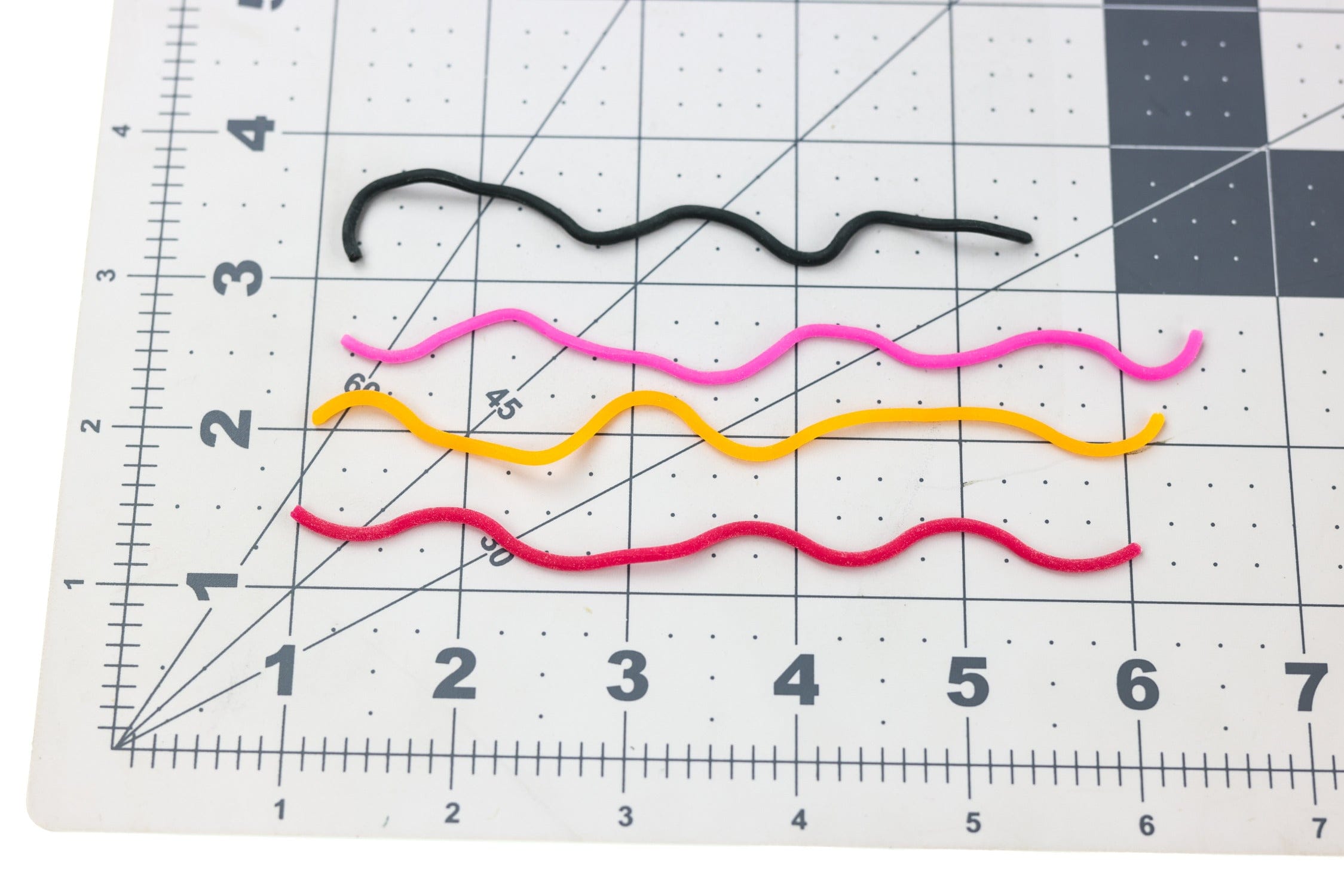 Hareline Caster's Squirmito soft rubber squirmers in black, pink, yellow and red on gridded cutting mat for fly tying
