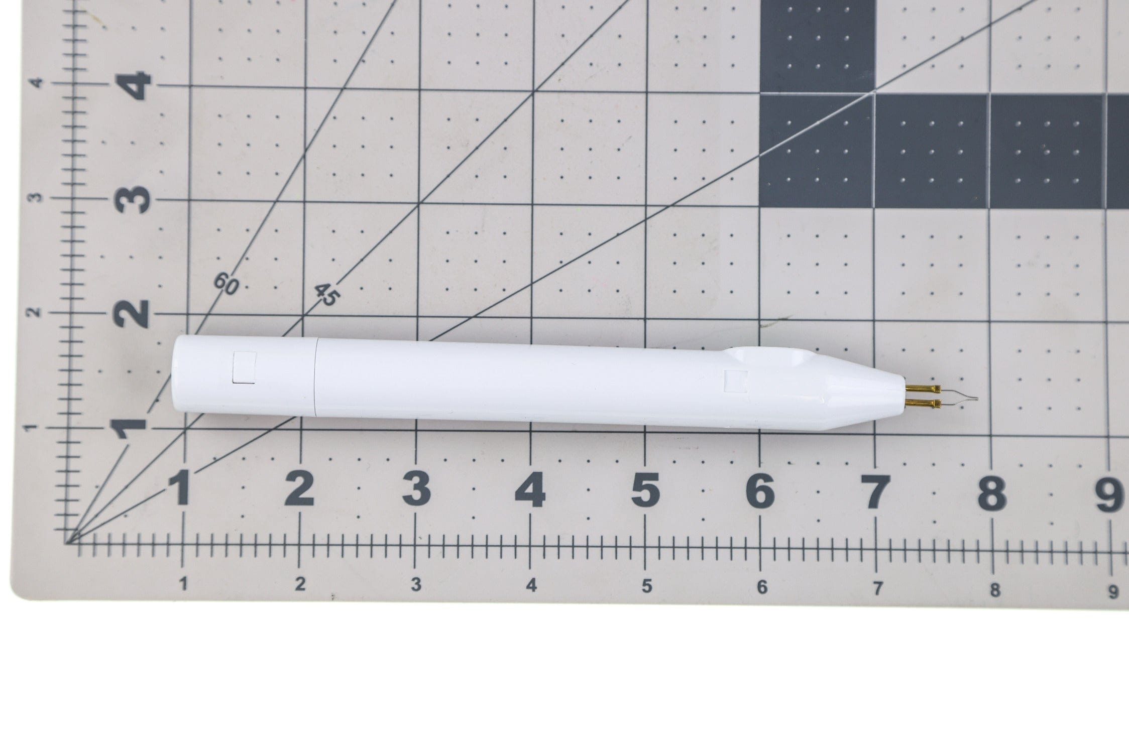 Hareline white plastic pen-style cautery tool with gold tips on gridded mat for fly tying