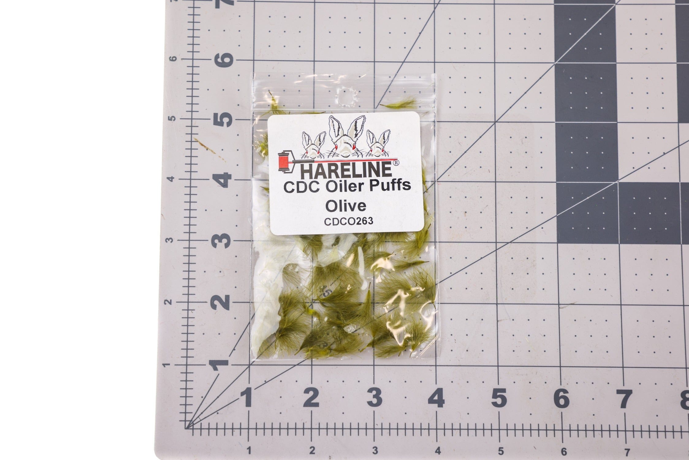 Olive CDC oiler puffs - olive feather clusters in clear plastic bag with label on gridded cutting mat, fly tying material