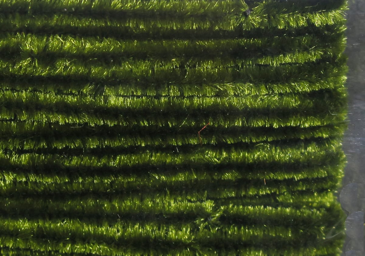 Olive green Hareline chenille, shiny fuzzy synthetic yarn in parallel ribbed strands for fly tying