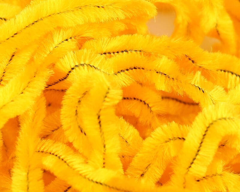 Bright yellow chenille strands with fuzzy pile and black stitched core, soft fly tying material