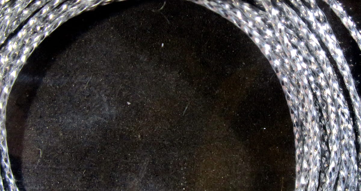 Silver braided synthetic chironomid braid coiled on black background for fly tying