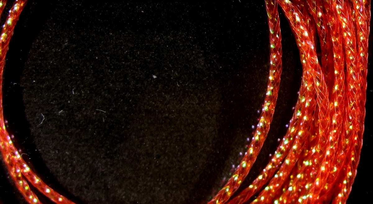Hareline chironomid braid, bright red braided synthetic with green-gold iridescent flash, fly tying material coiled on black