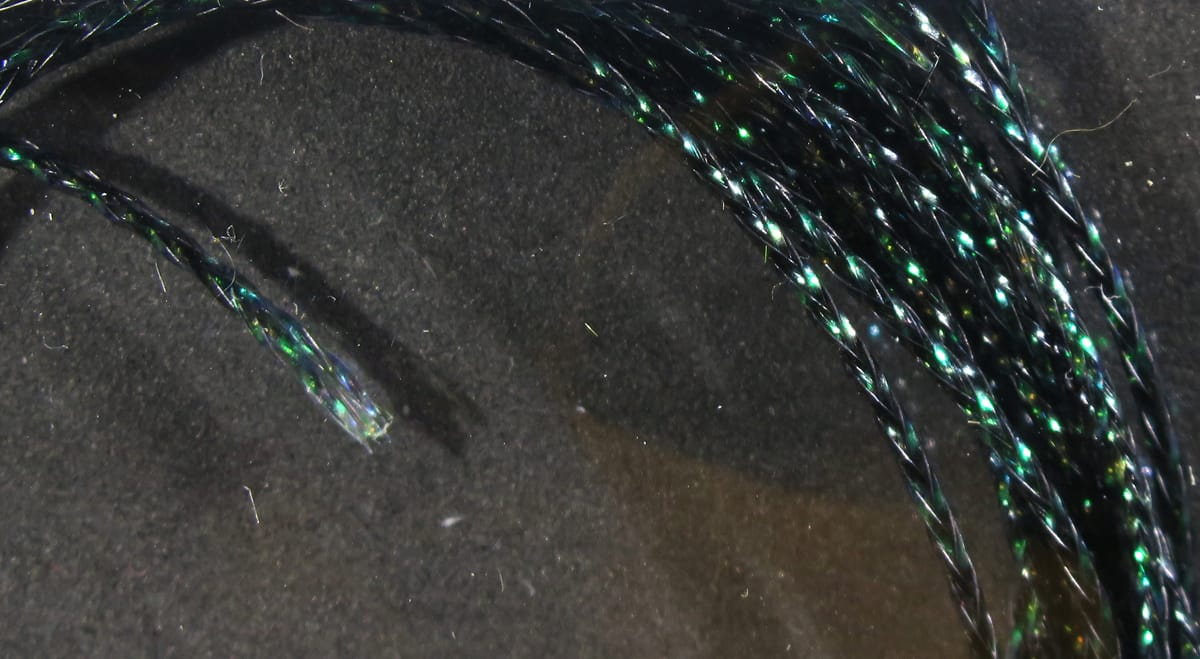 Hareline chironomid braid close-up: black braided synthetic strands with green iridescent tinsel for fly tying
