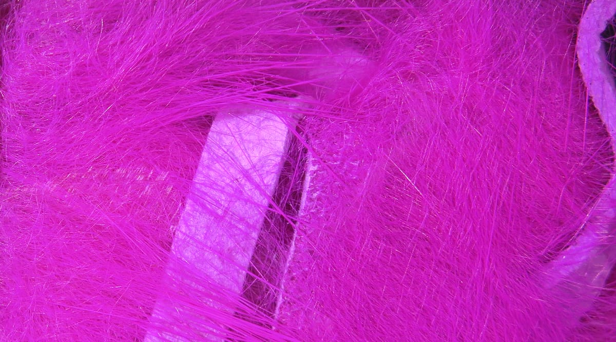 Hot pink Hareline crosscut rabbit fur strips showing long fluffy fibers and fabric backing for fly tying
