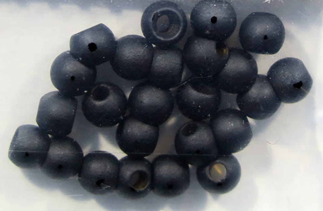 Matte black round brass beads with center holes for fly tying, scattered in a clear plastic pack