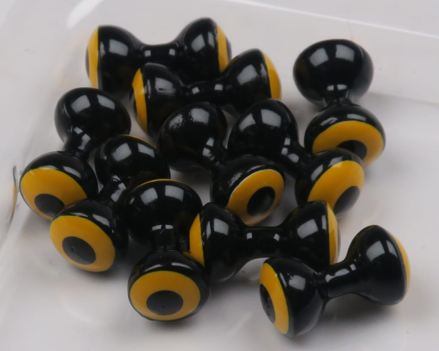 Glossy black double-pupil brass eyes with yellow ring and black center, dumbbell shape for fly tying