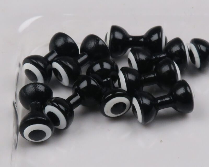 Glossy black double-pupil brass eyes with white concentric rings, dumbbell-shaped for fly tying