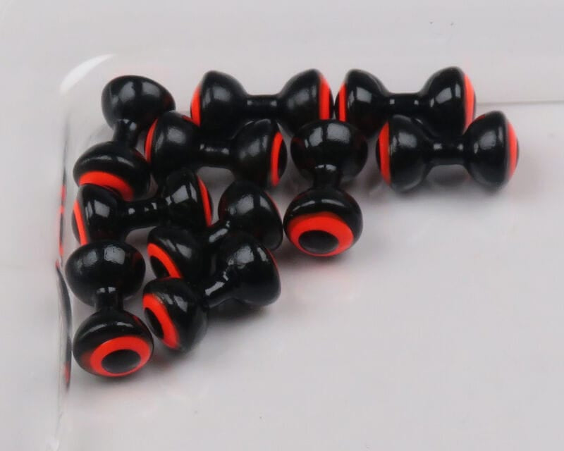 Glossy black double-pupil lead eyes with bright red-orange concentric rings and hollow centers for fly tying.