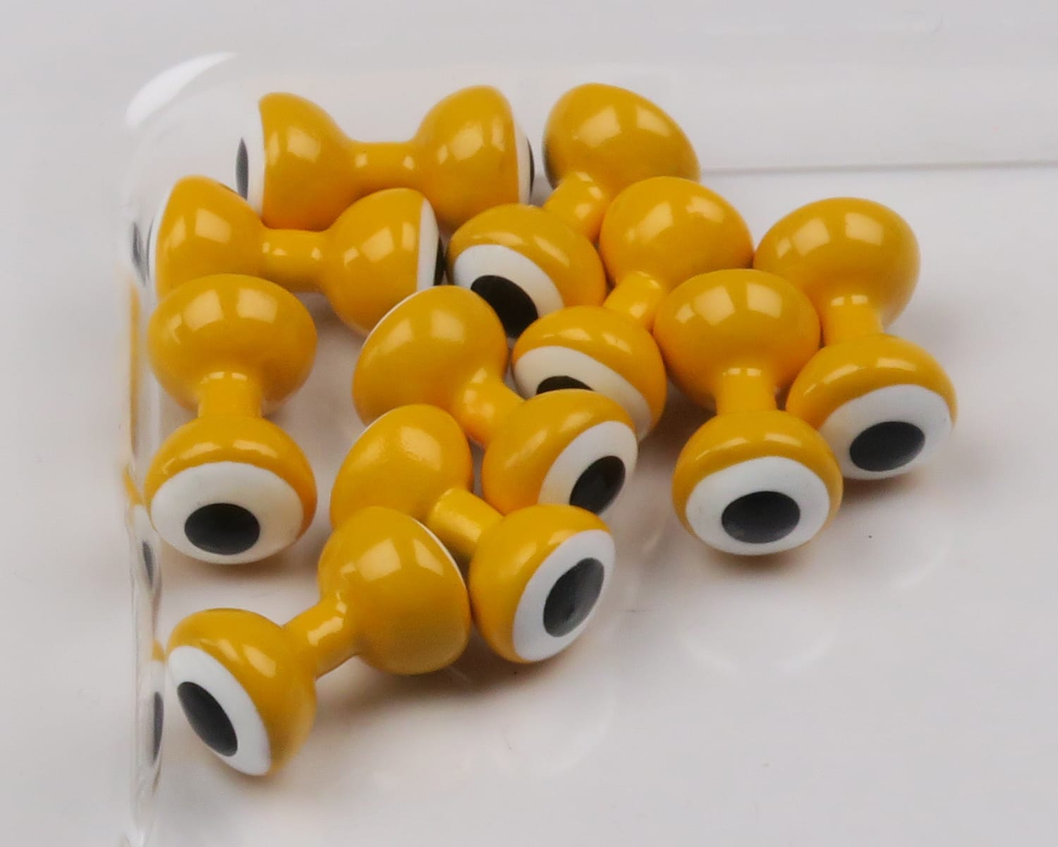 Glossy mustard-yellow double-pupil lead eyes with white rings and black centers, clustered for fly tying craft