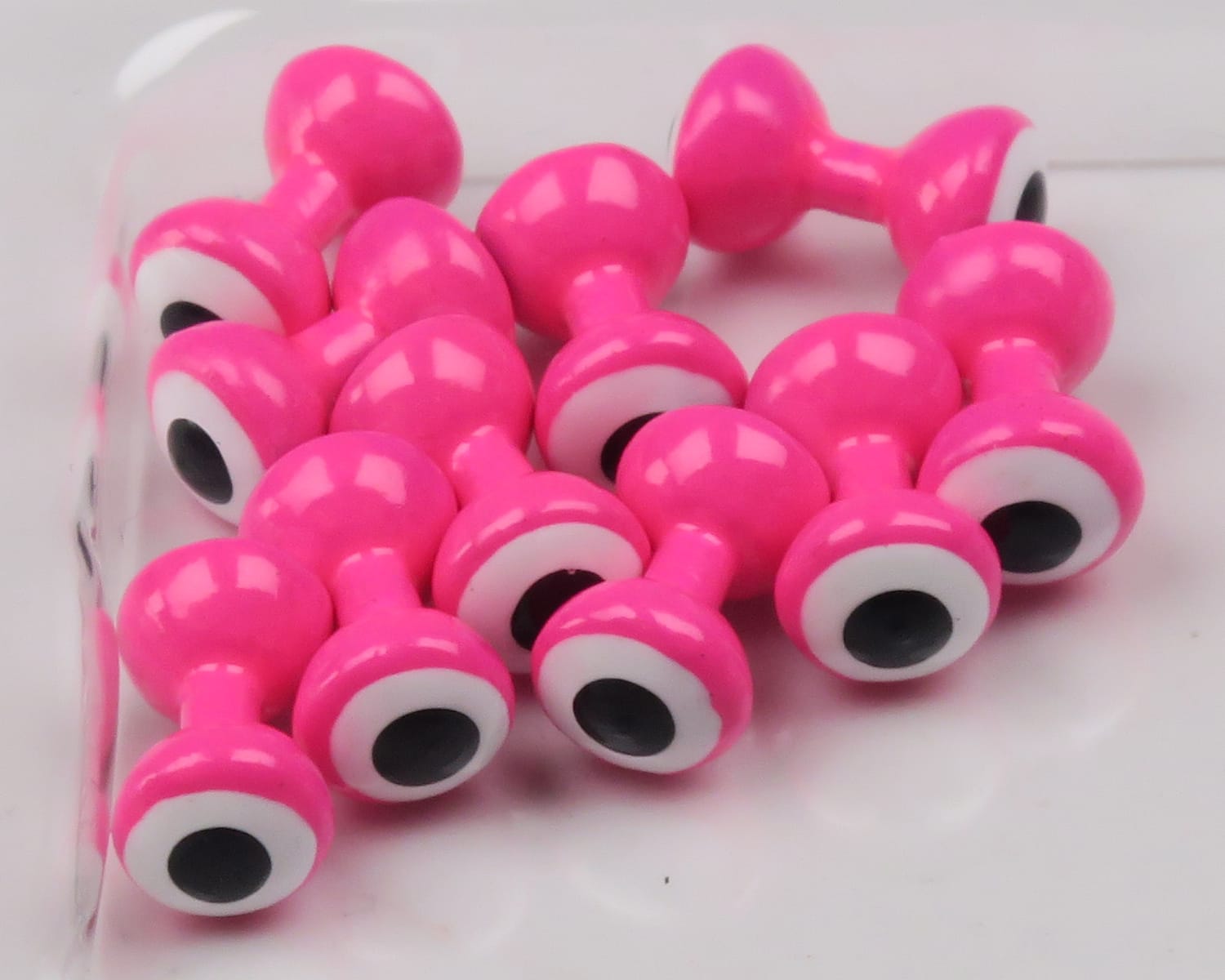 Bright pink Hareline double-pupil lead eyes with white and black pupils, glossy painted metal fly tying eyes