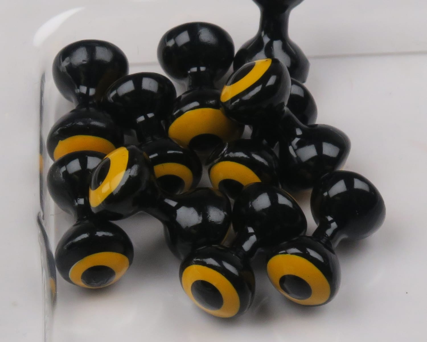 Glossy black double-pupil lead eyes with yellow rings for fly tying, bulbous two-lobed Hareline lead eyes clustered