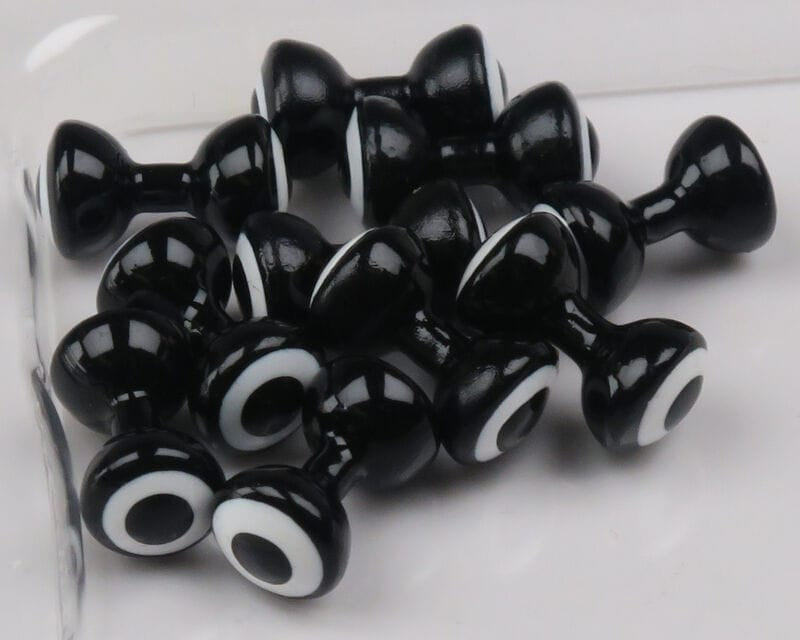 Multiple glossy black double-pupil lead eyes with white concentric rings, barrel-shaped fly tying eyes by Hareline