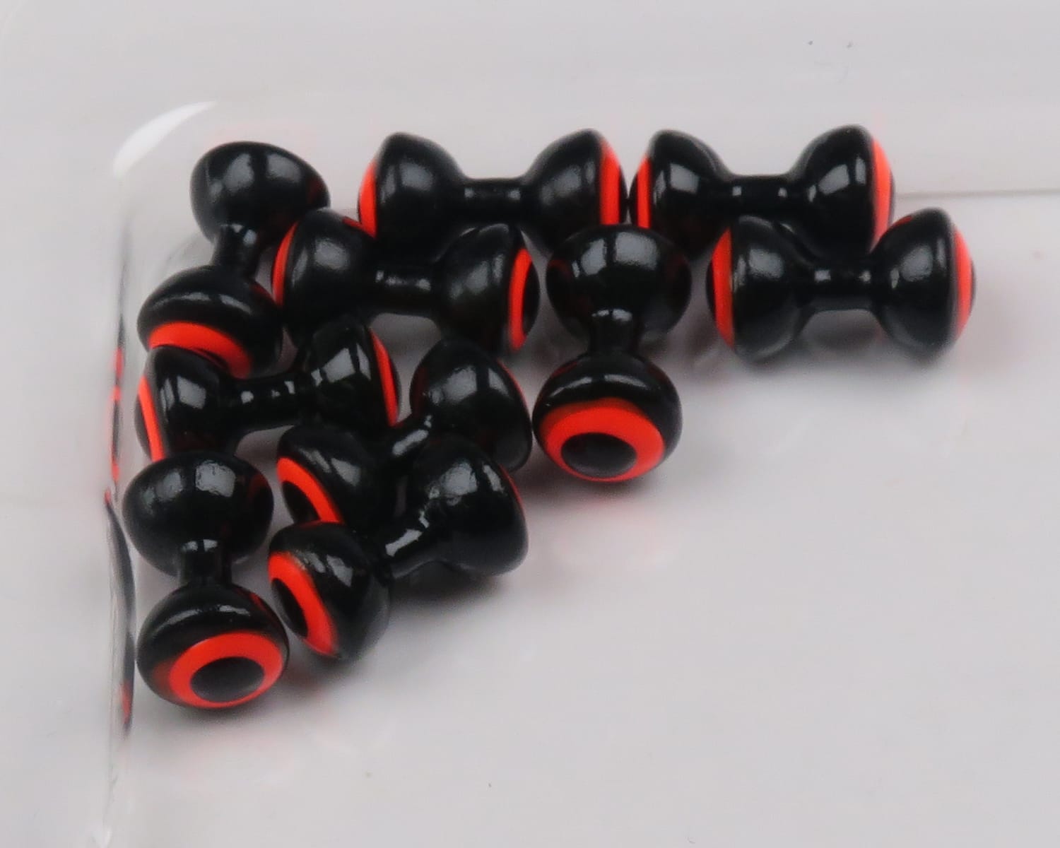 Glossy black double-pupil lead eyes with bright orange rings, hourglass style for fly tying