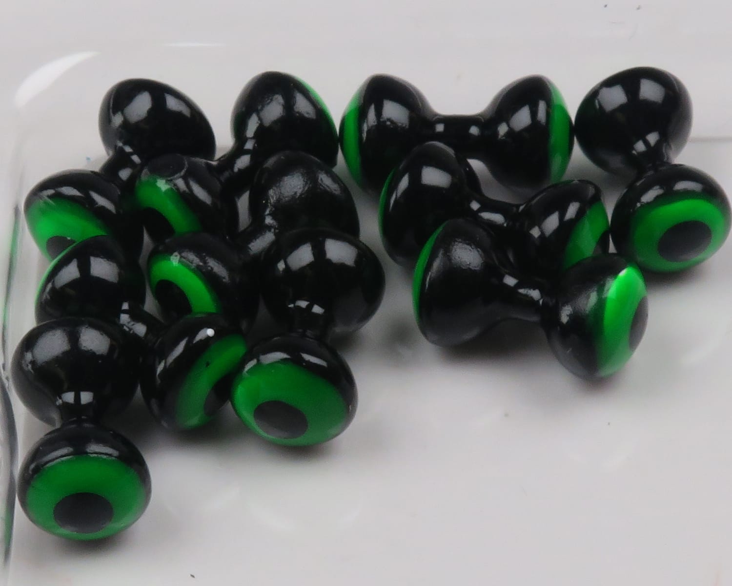 Glossy black double-pupil lead eyes with bright green rings, dumbbell style for fly tying