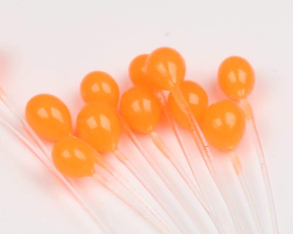 Bright orange epoxy crab eyes on clear mono stems for fly tying, glossy teardrop beads clustered together