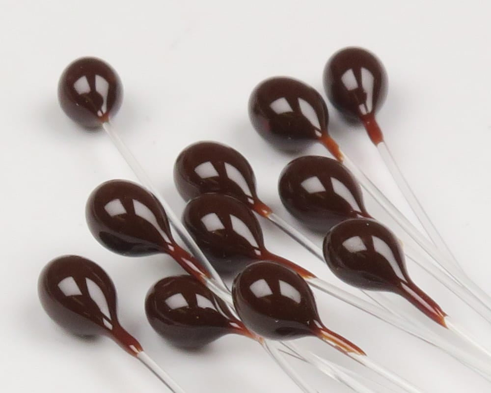 Glossy dark brown epoxy crab eyes on clear mono stems for fly tying, teardrop shapes with reflective highlights