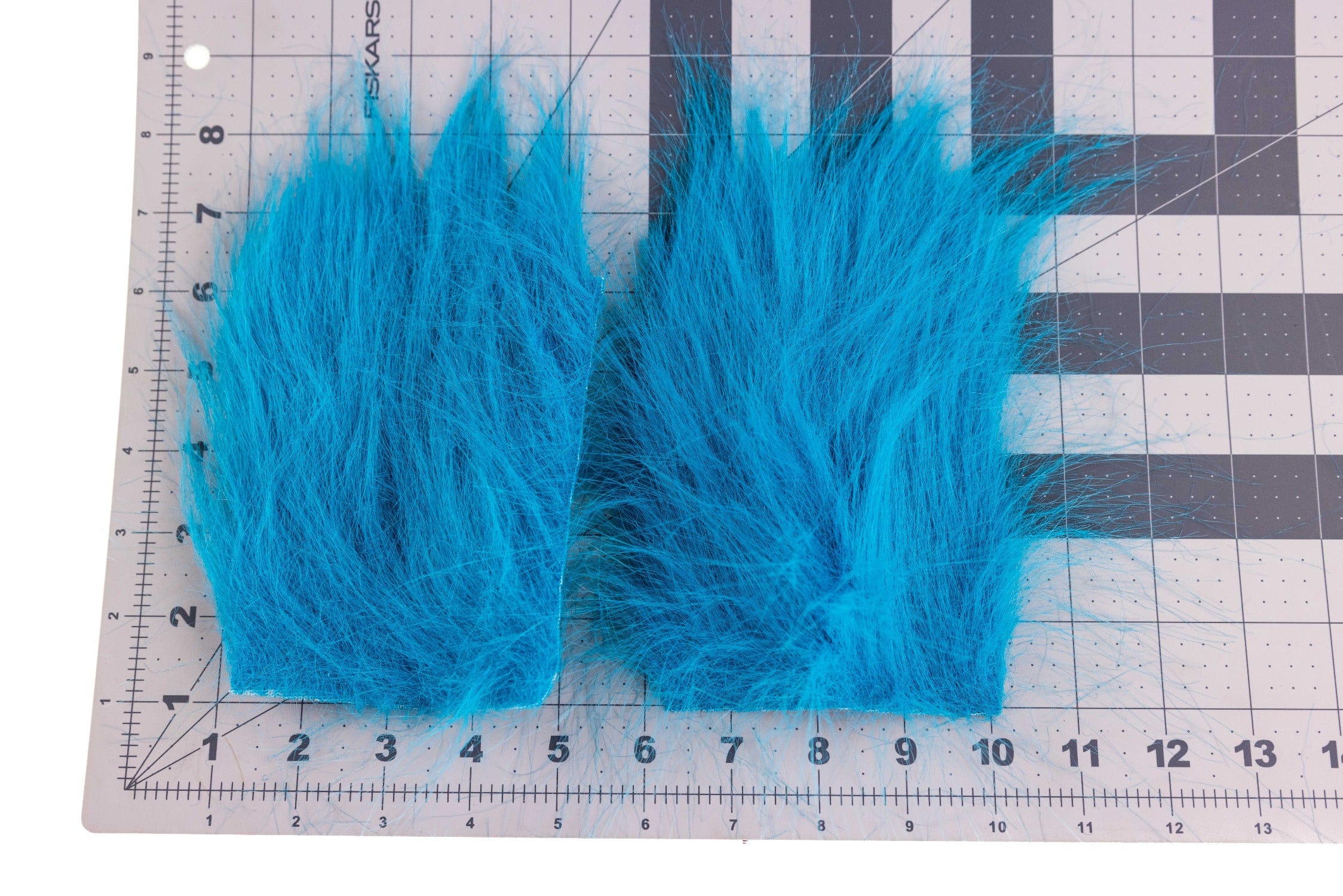 Bright turquoise long-pile craft fur strips laid on gridded cutting mat with ruler, ideal for fly tying