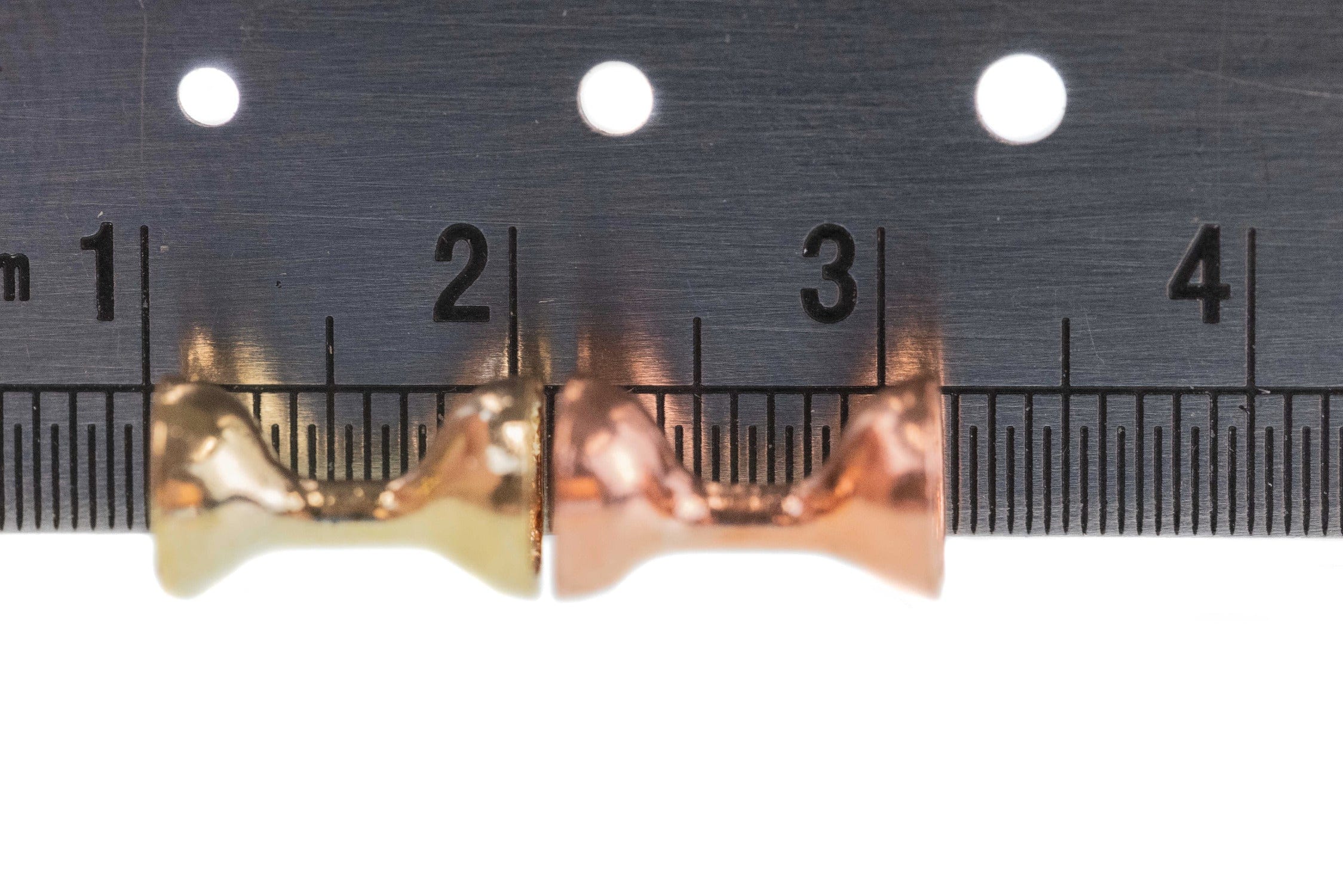 Gold and copper flat-end tungsten hour glass eyes on ruler showing size 2-4 for fly tying