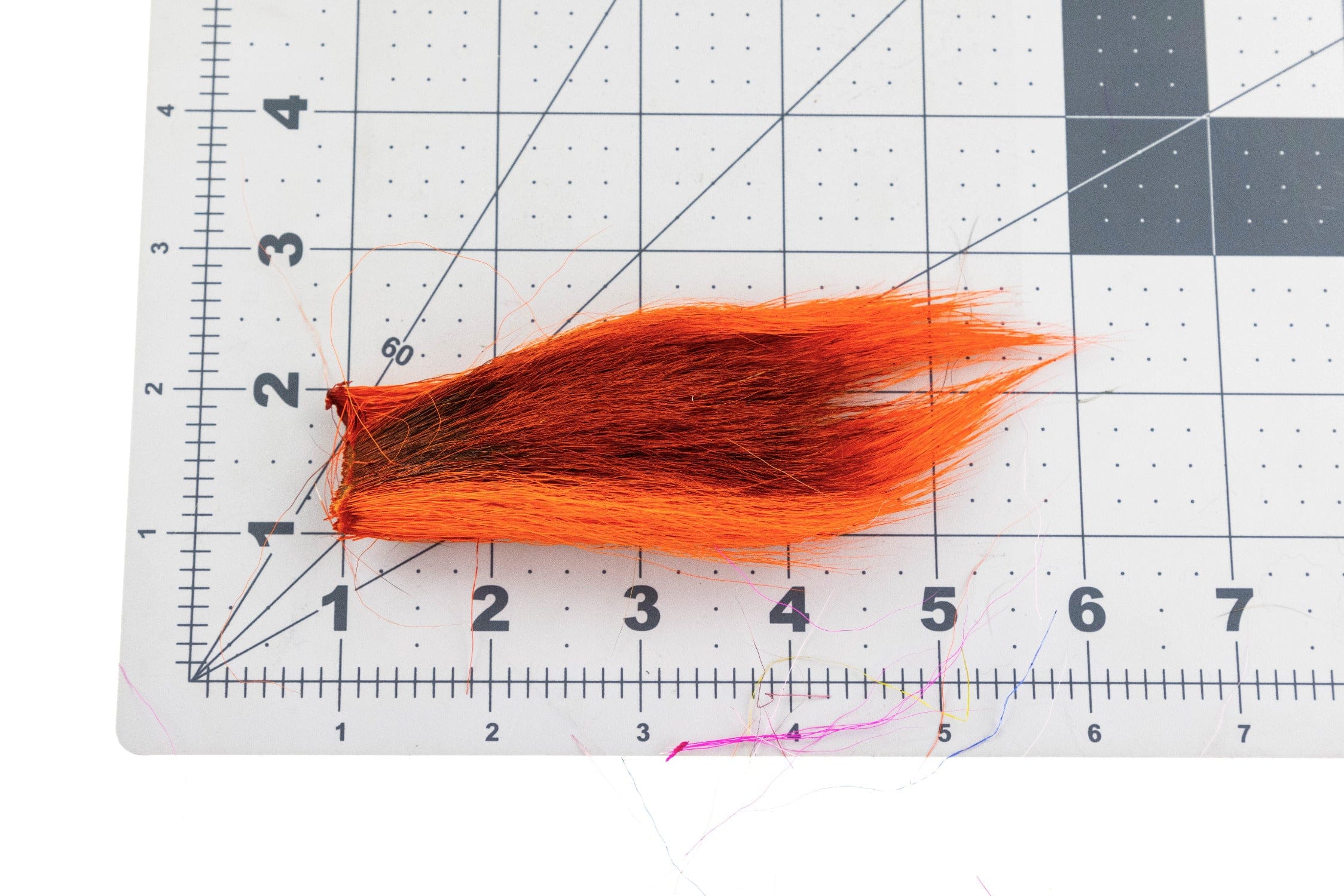 Fluorescent orange bucktail with dark brown underfur, long tapered strands laid on a cutting grid, fly tying material