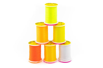 Stacked spools of Hareline Glo-Brite floss in fluorescent yellow, orange and white on plastic spools for fly tying