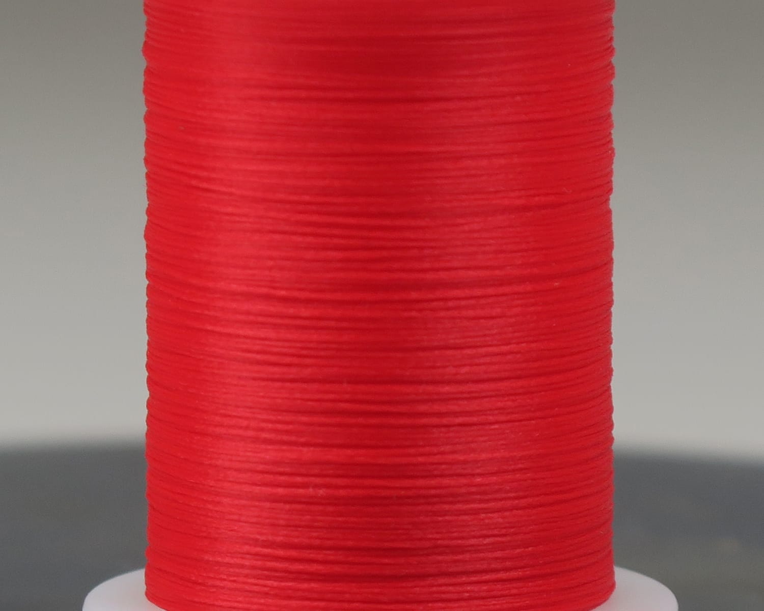 Hareline Glo-Brite bright red synthetic floss spool for fly tying, smooth glossy thread close-up