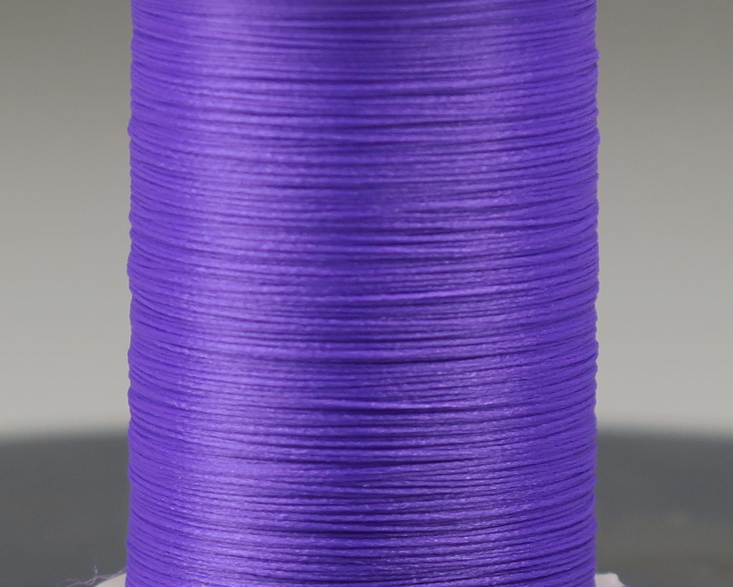 Bright purple Glo-Brite floss wound on spool, smooth glossy synthetic thread for fly tying