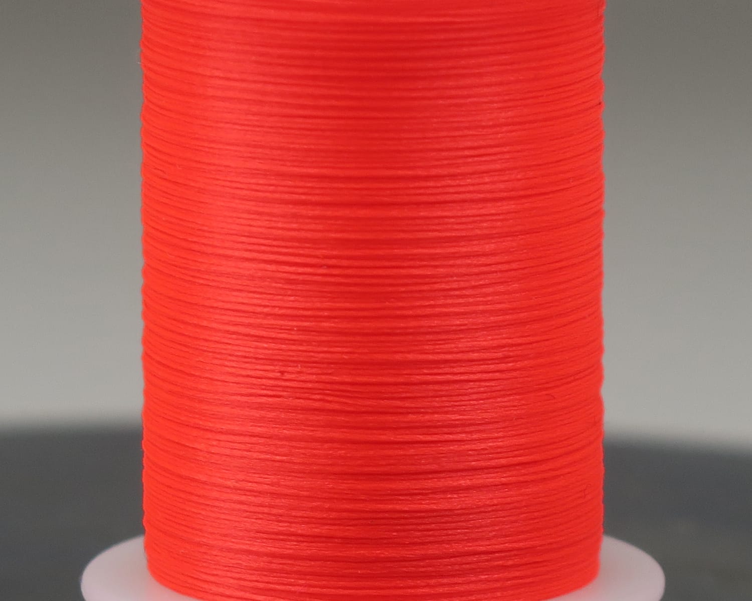 Bright fluorescent orange Hareline Glo-Brite synthetic floss spool for fly tying, smooth glossy nylon thread close-up