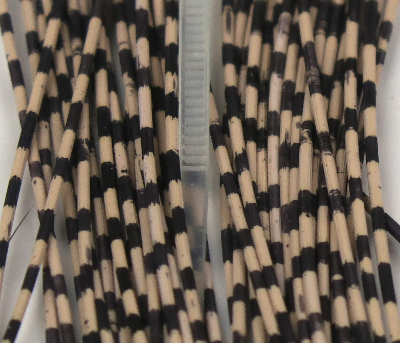 Tan and black grizzly-barred rubber legs for fly tying, thin flexible striped rubber strands in a compartment tray