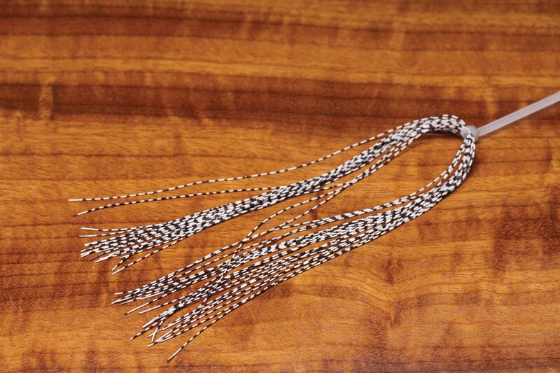 Hareline grizzly barred rubber legs, black-and-white barred elastic strands looped at one end for fly tying on wooden surface