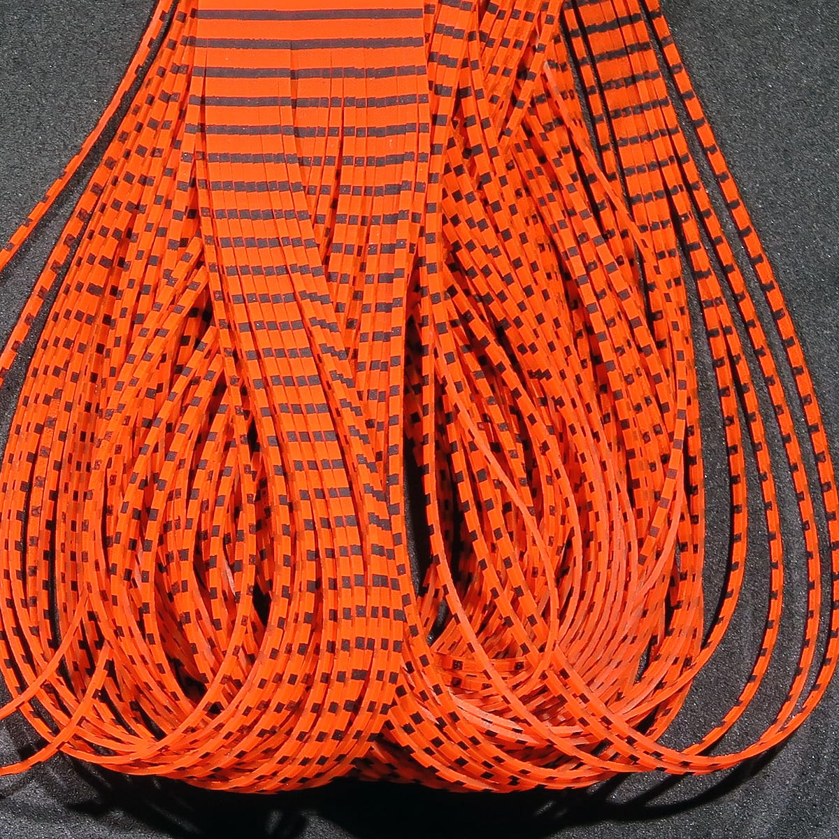 Bright orange Hareline grizzly flutter legs for fly tying, thin flexible rubber strands with black striped grizzly pattern