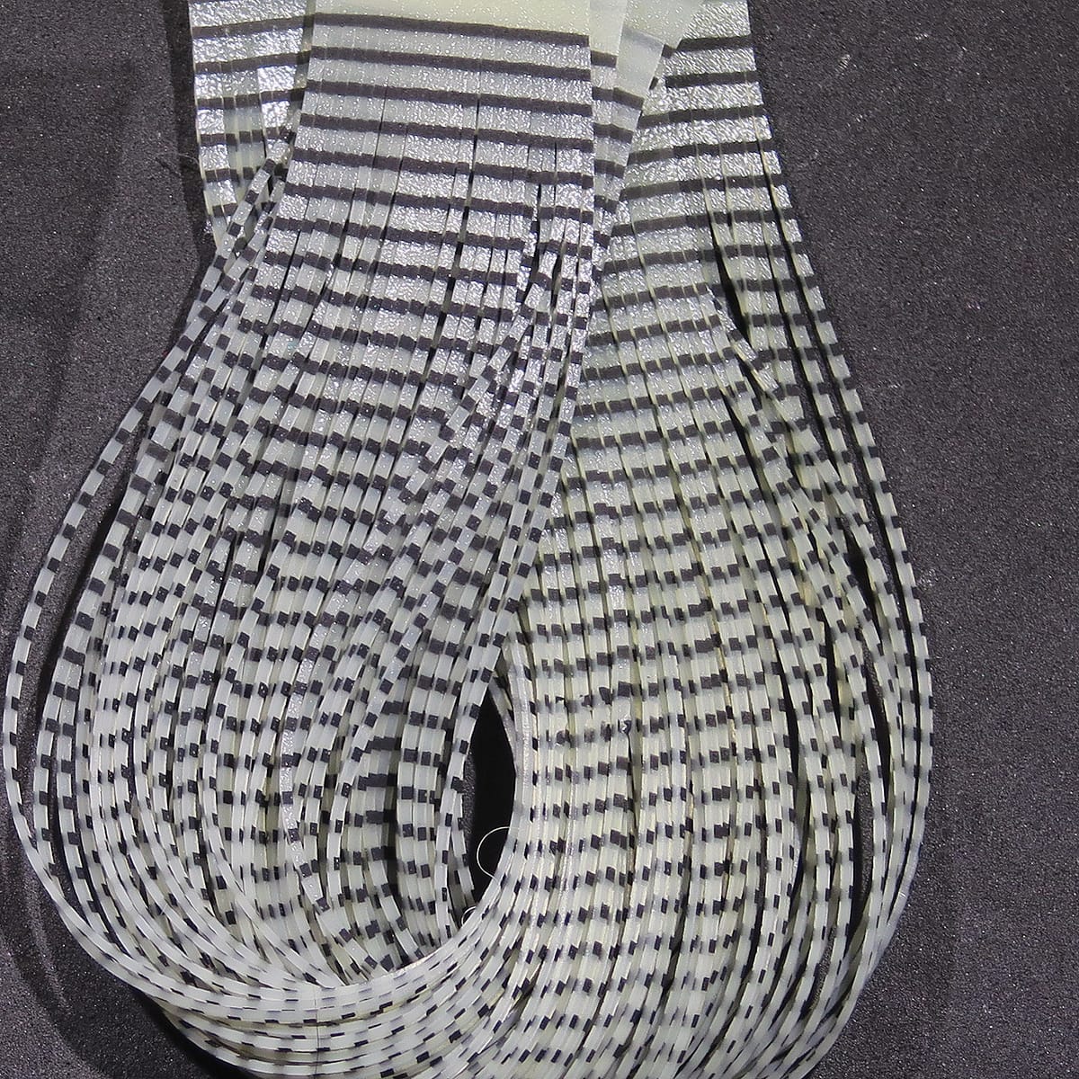 Hareline Grizzly flutter legs, bundled translucent white-gray strips with black barred grizzly pattern for fly tying