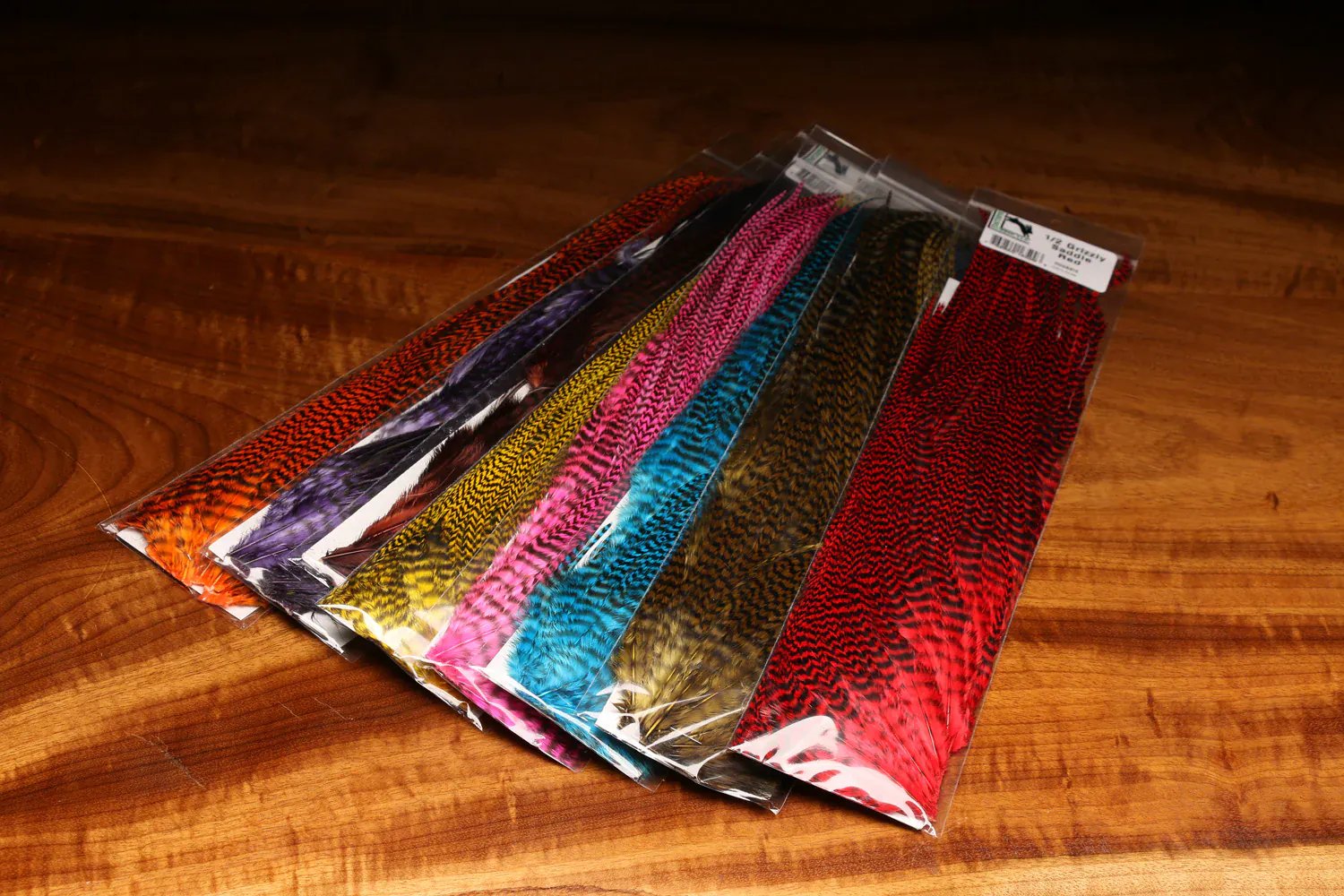 Hareline grizzly half saddle fly tying feathers, dyed grizzly hackle in red, blue, yellow, pink and orange packages on wood