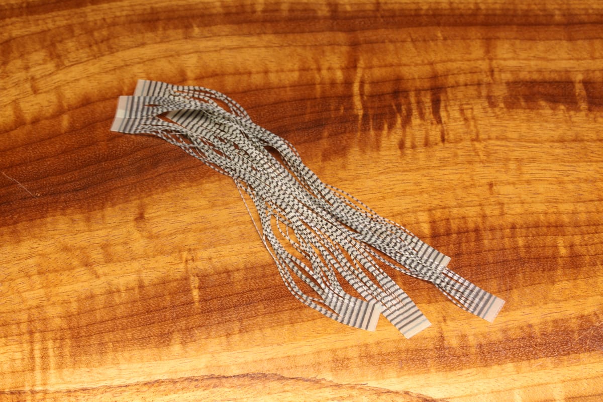 Gray and black grizzly-pattern synthetic micro legs for fly tying, multiple thin flexible strips on wood background