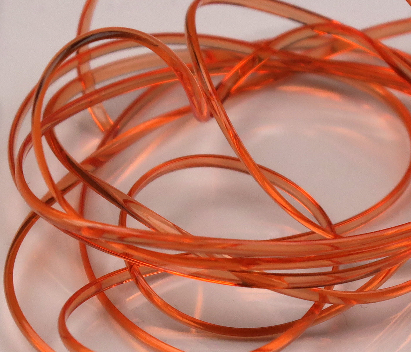 Translucent orange half-round D-rib coiled strands for fly tying, glossy flexible plastic ribbing