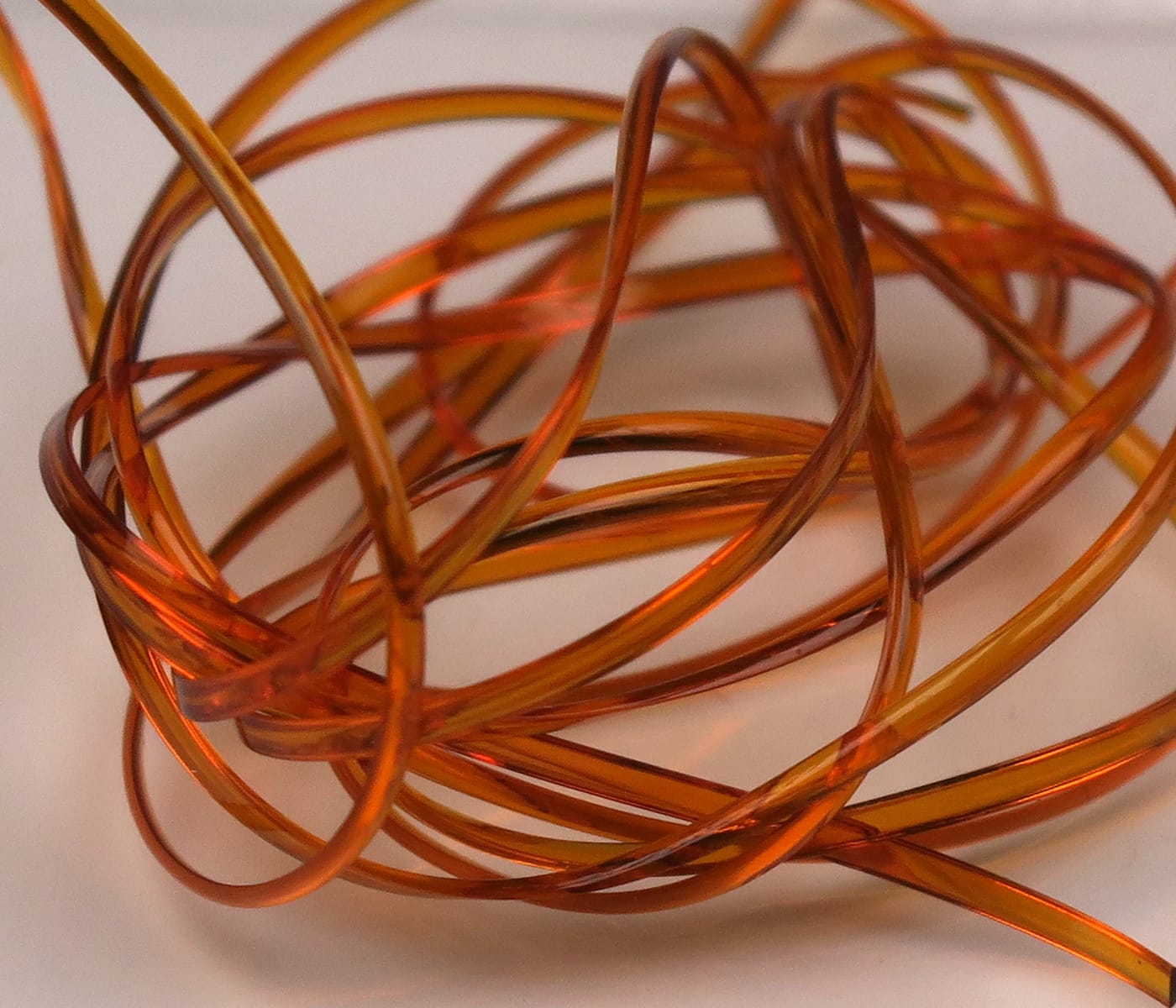 Translucent amber-orange half-round D-rib coiled strands, glossy plastic rib material for fly tying