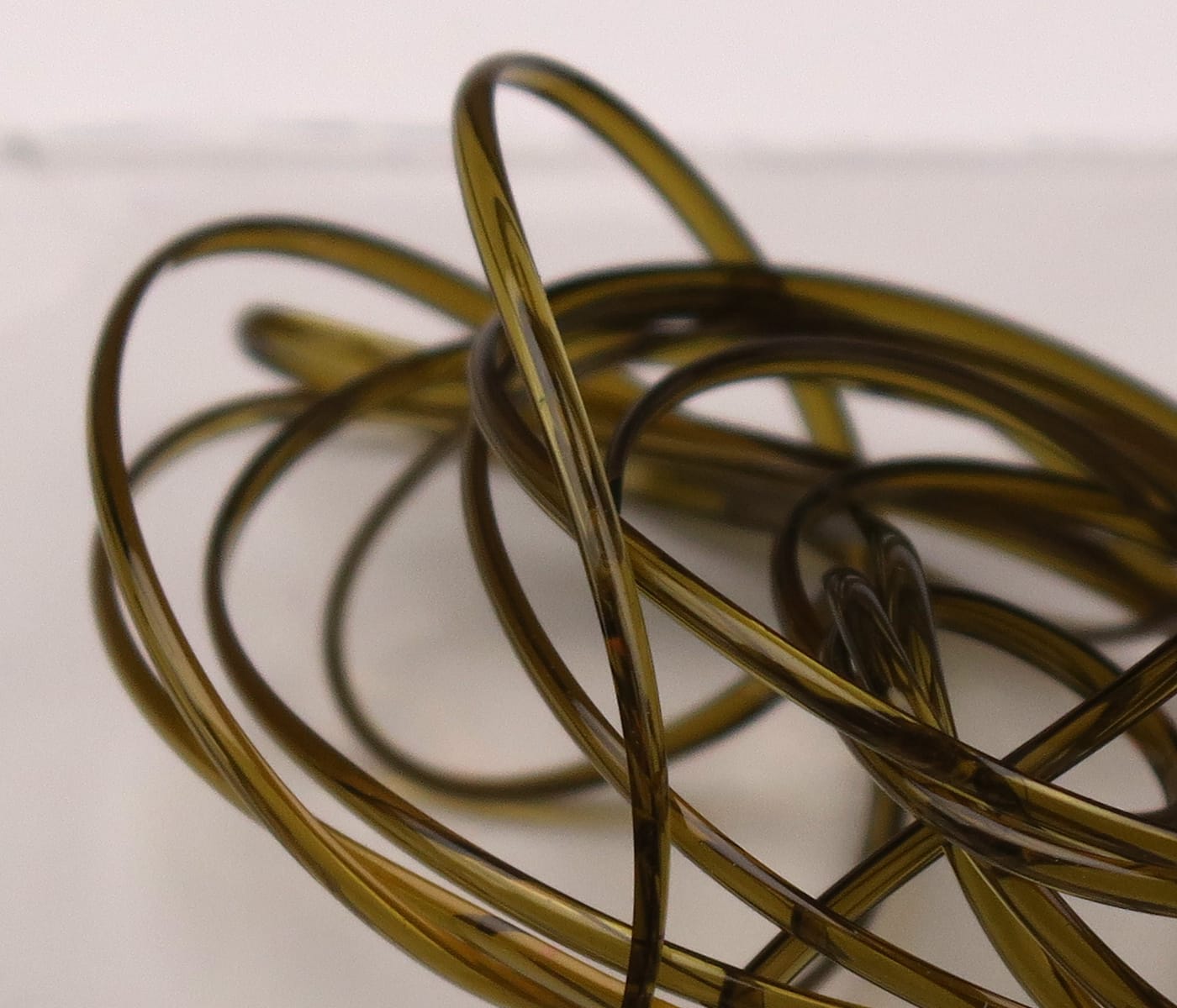Translucent olive-brown half-round D-rib coiled tubing used for fly tying, glossy plastic rib material in tangled loops