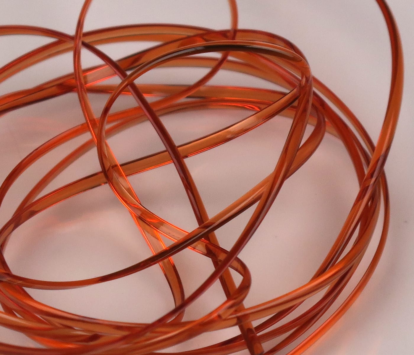 Translucent copper-orange half-round D-rib coil, glossy plastic ribbing for fly tying