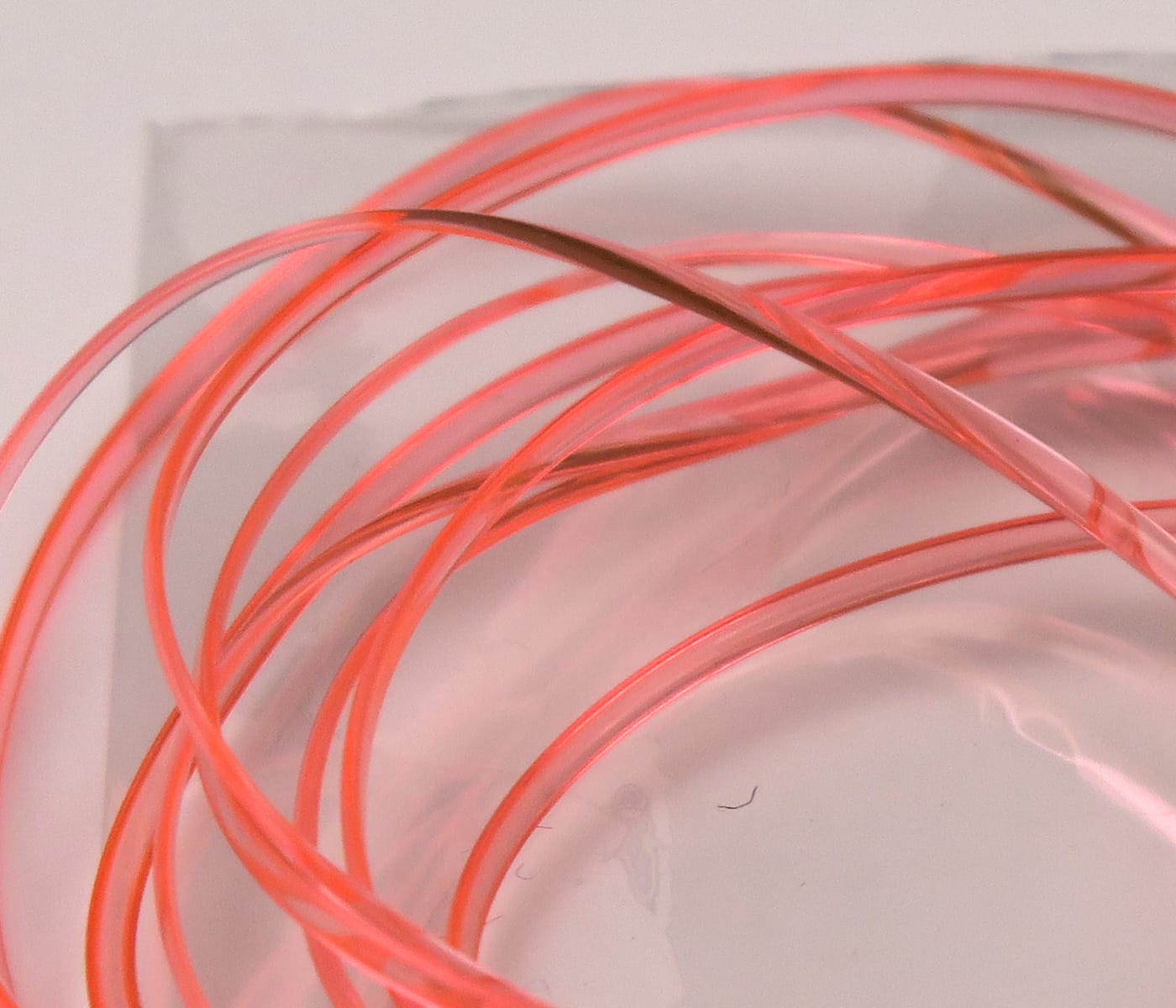 Translucent coral pink Hareline half-round D-rib coiled strands, smooth plastic fly tying rib for body segmentation