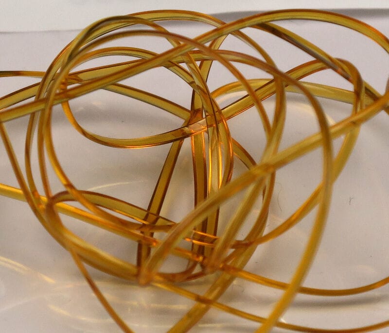 Hareline half-round D-rib translucent amber plastic ribbing coiled for fly tying on a white surface