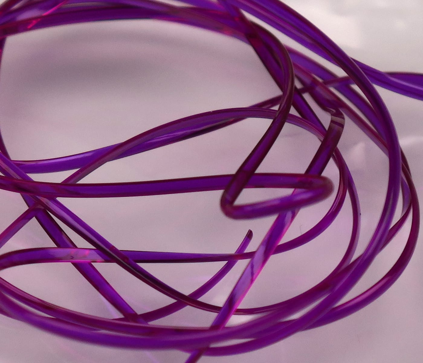 Translucent purple half-round D-rib coiled strands, glossy plastic fly-tying rib material with semi-flat profile