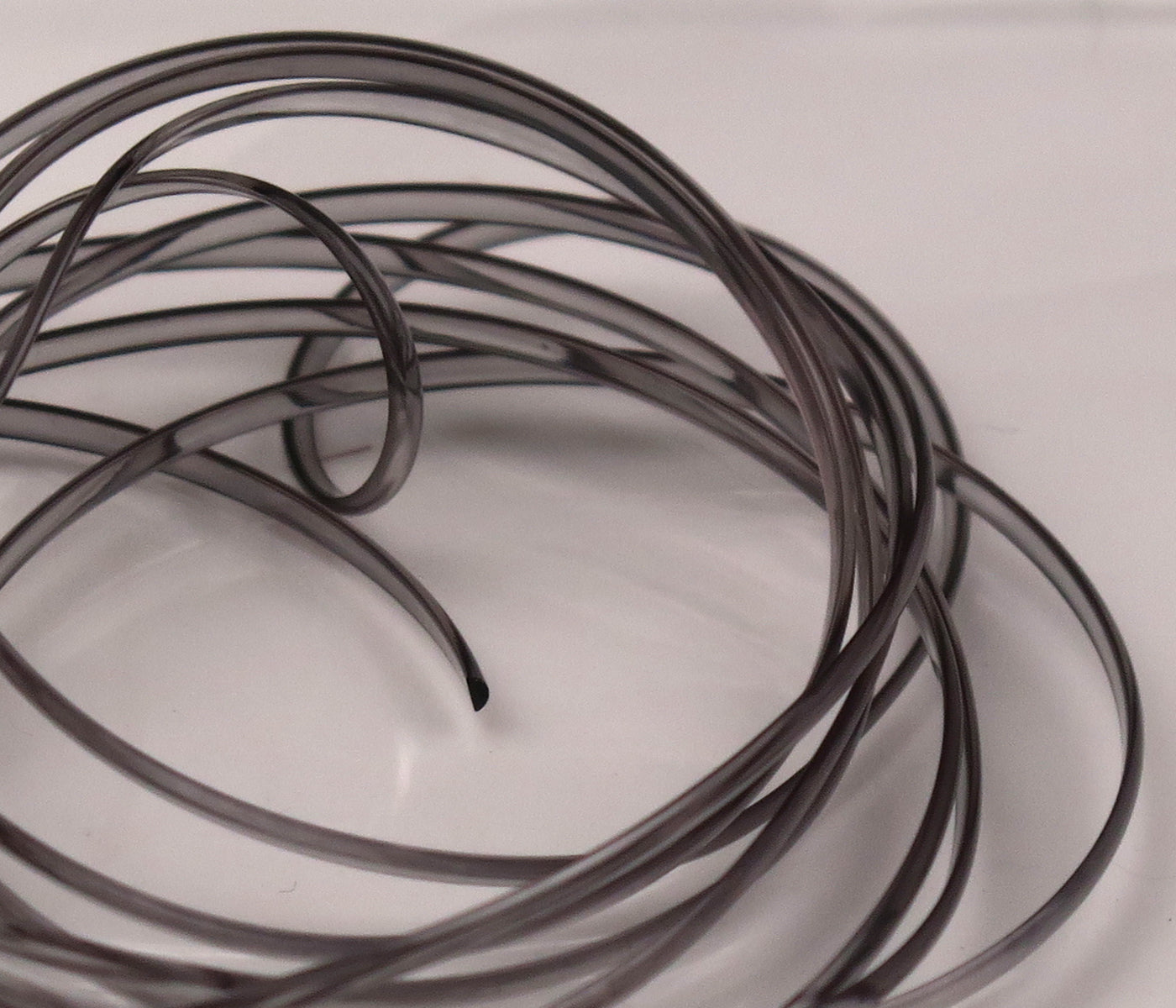 Coiled translucent smoke-gray Hareline half-round D-rib tubing for fly tying, thin D-shaped rib material