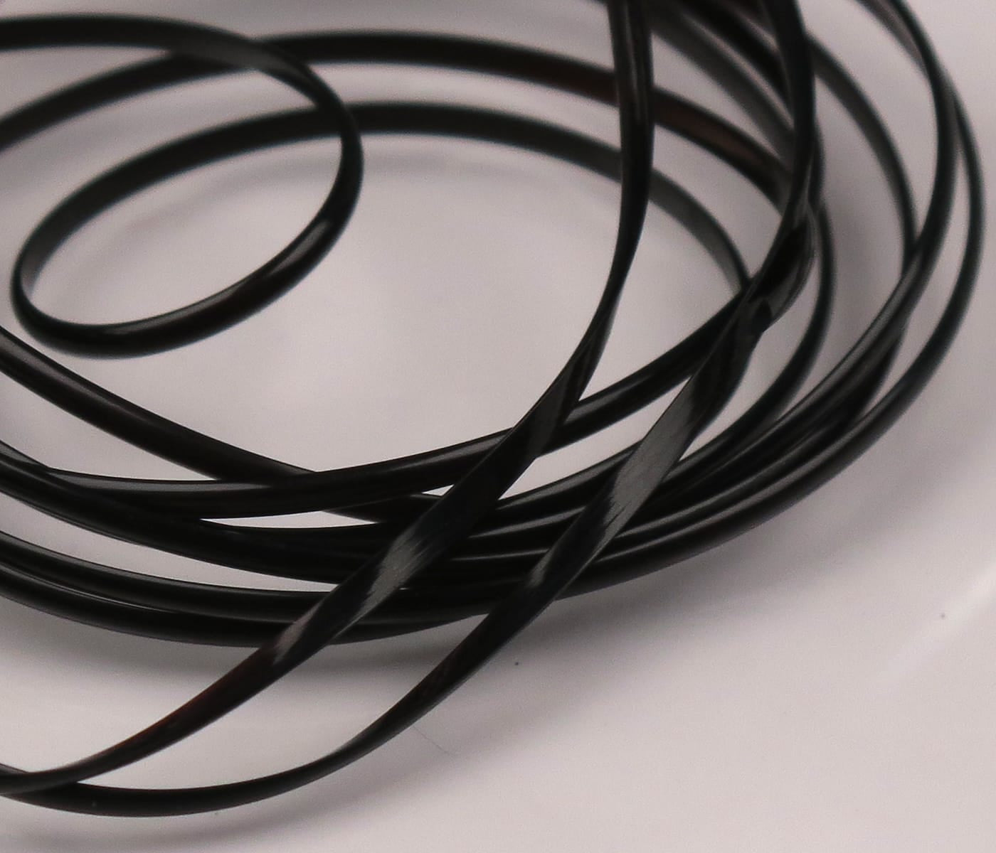 Glossy black Hareline half-round D-rib for fly tying, coiled thin semi-circular plastic rib on white background