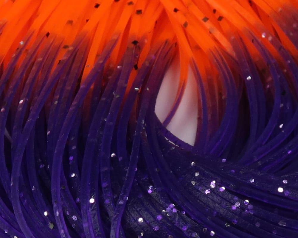 Close-up fly tying rubber legs: hot-tipped orange to purple synthetic strands with glitter flecks
